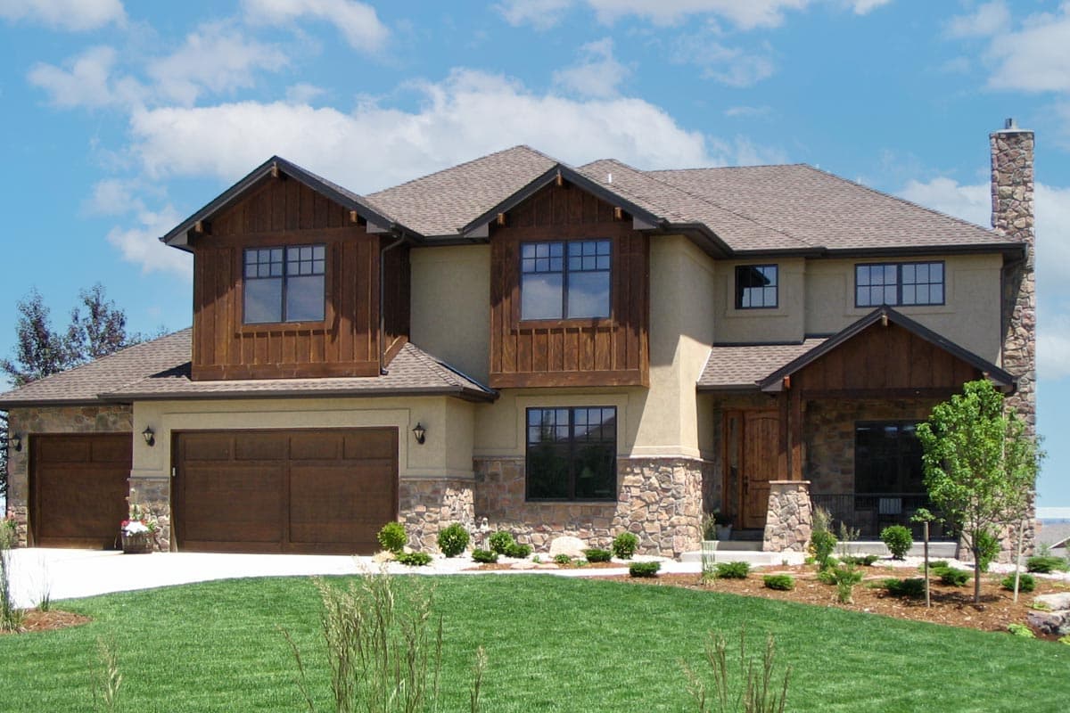 House plan exterior. Two-story home with Craftsman-style detailing. Features include a stone chimney, gabled roof, and wood-clad dormers.
