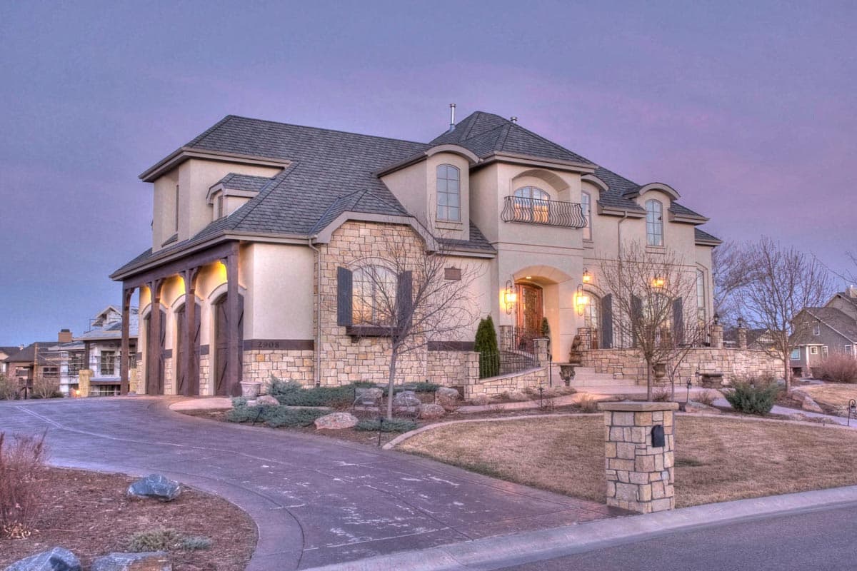 House plan exterior: Two-story home with stone accents, covered entry, arched windows, and a multi-car garage with wood doors.