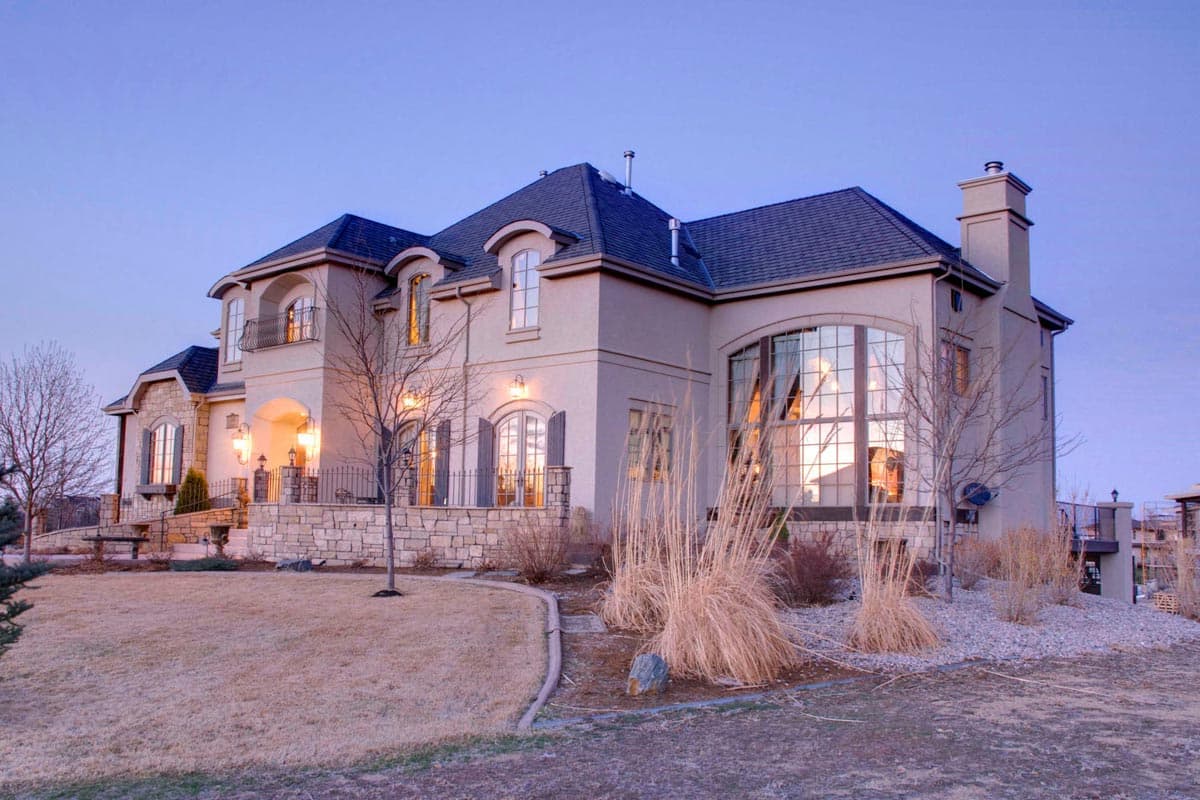 House plan exterior: Large two-story home with arched windows, dormers, and a prominent stone-clad base.