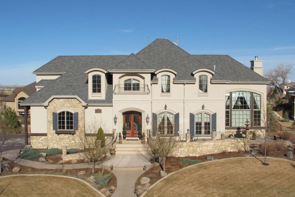 French-inspired house plan exterior with mansard roof, stone accents, arched dormers, and a prominent arched entryway.