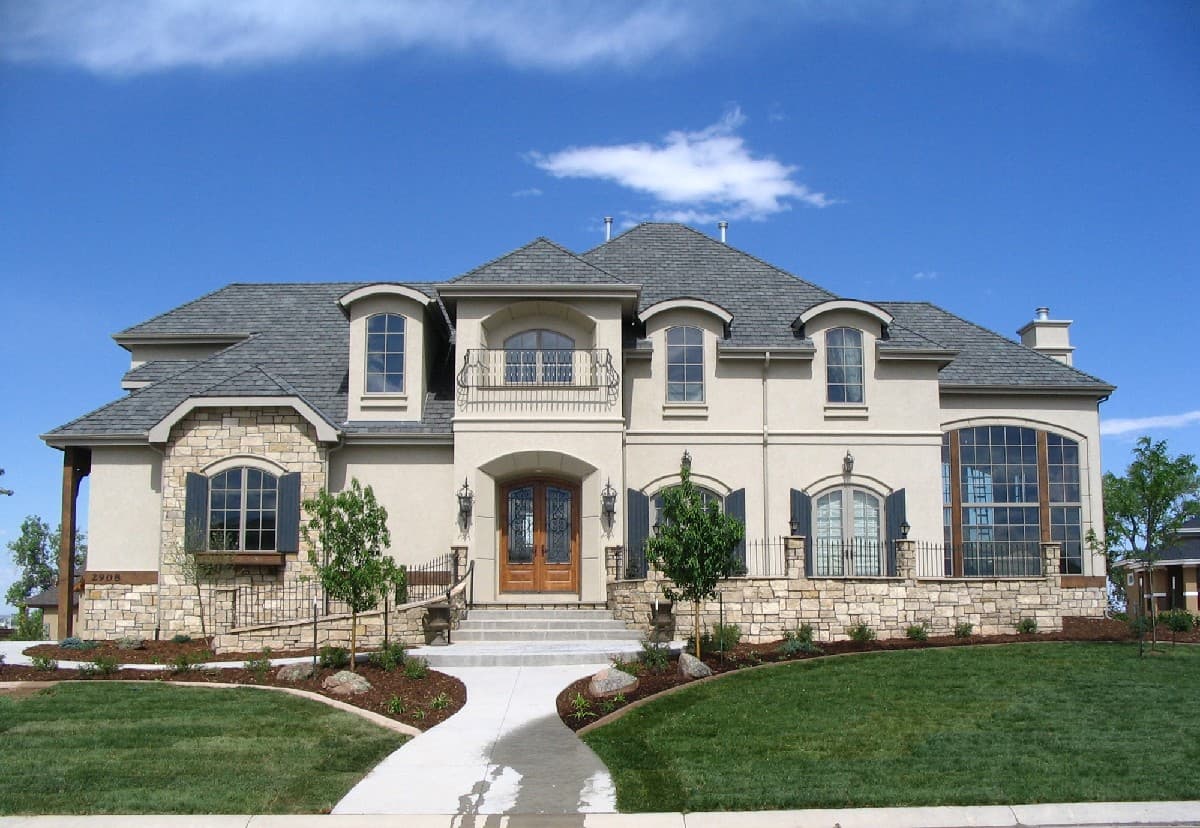 House plan exterior: Two-story home with stone accents, arched windows, dormers, and a second-story balcony over the entrance.