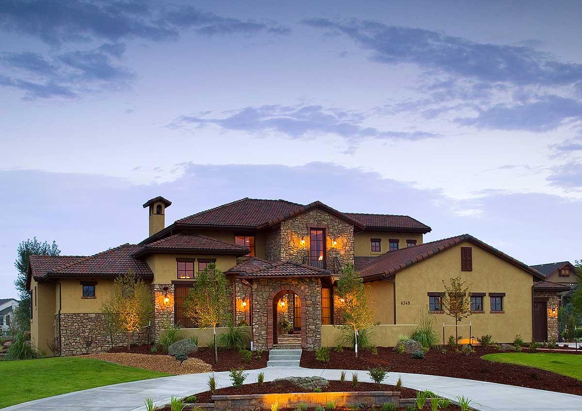 House plan exterior with arched stone entryway, tile roof, multiple gables, stone accents, and exterior lighting.