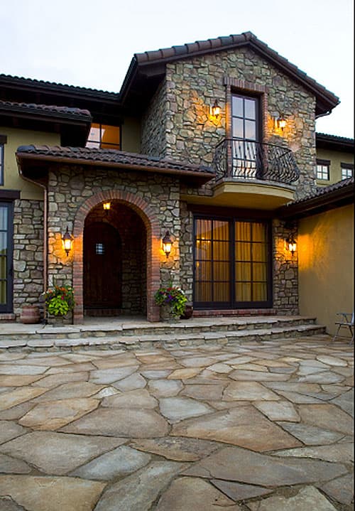 House plan exterior with arched entry, stone facade, second-story balcony, and tiled roof.
