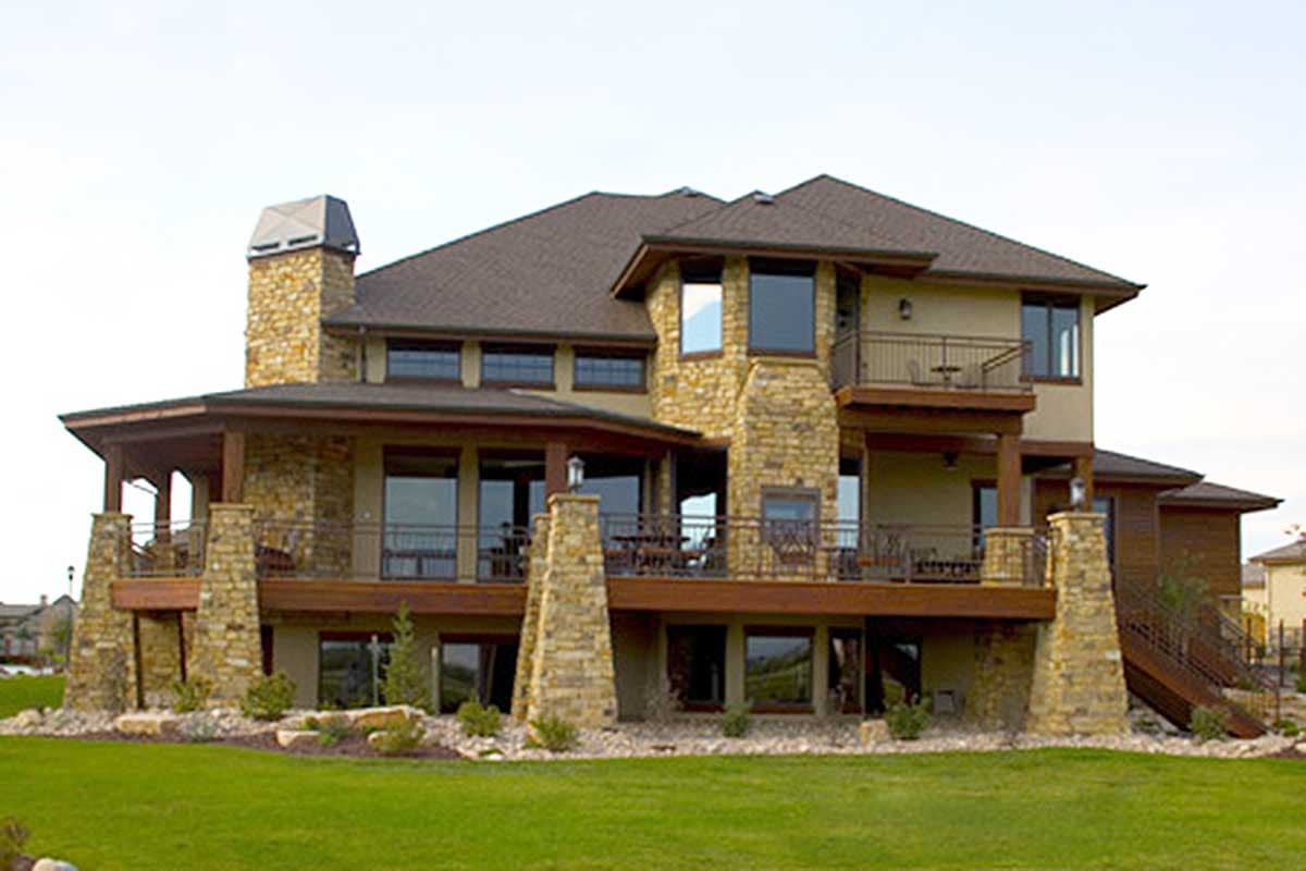 House plan exterior: Two-story residence with stone accents, multiple balconies, and a prominent stone chimney.