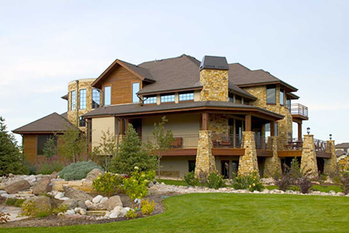 House plan exterior: multi-story home with stone accents, covered porches, wood siding, multiple gables, and a prominent stone chimney.