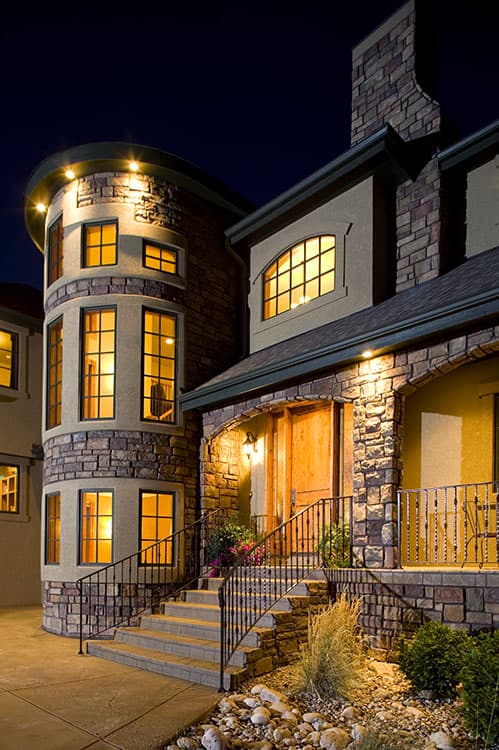 House plan exterior with stone facade, rounded tower, arched window above entrance, and curved staircase.