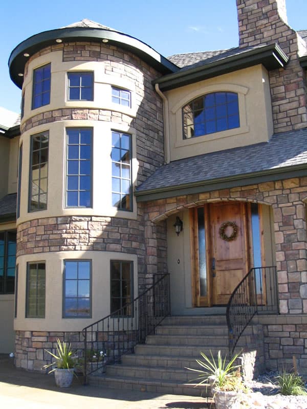 House plan exterior featuring a curved stone tower with multiple windows, arched window, and wood double front door.