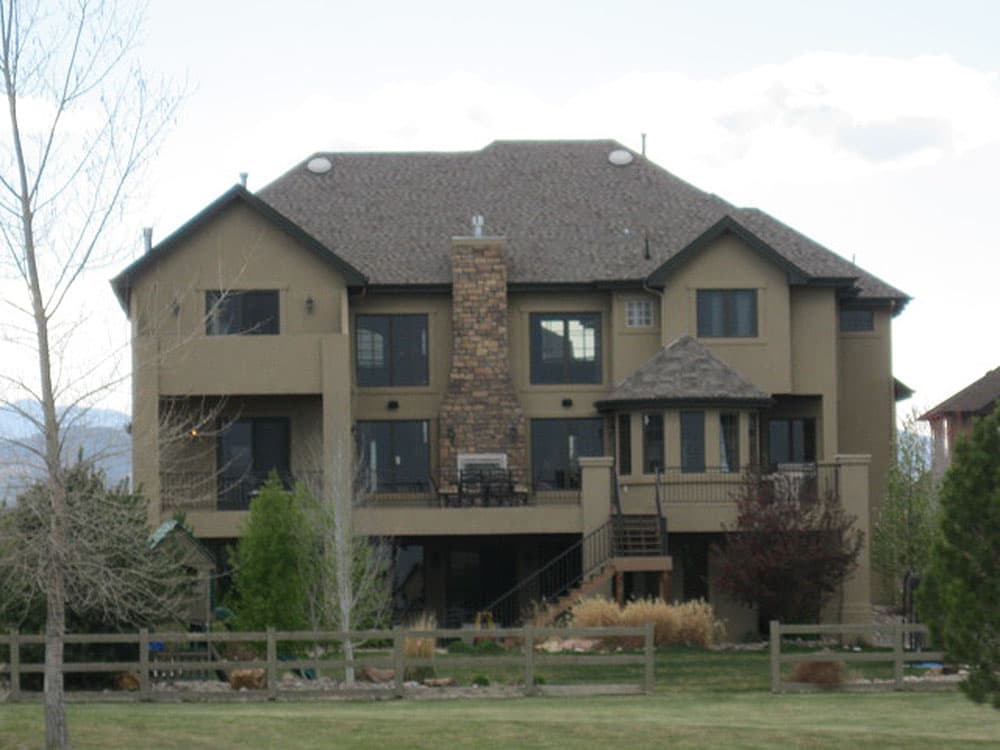 House plan exterior: two-story home with stone chimney, multiple gables, bay window, and rear deck.