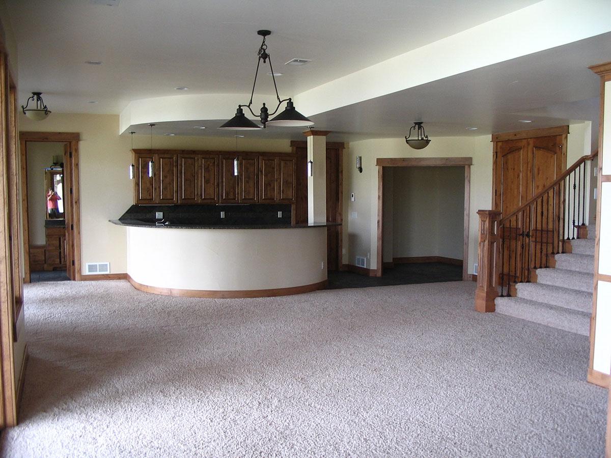 Interior view of a finished basement with a curved bar, wood cabinetry, carpet, and a staircase with iron railing.