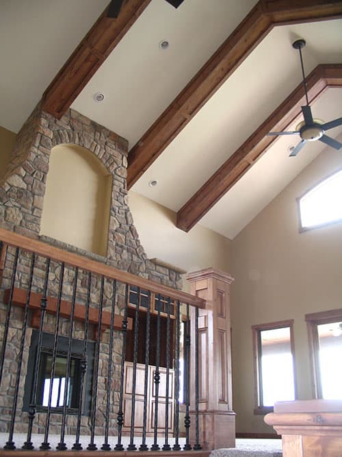 Interior view of great room with vaulted ceiling, exposed wood beams, stone fireplace, and wrought iron railing.