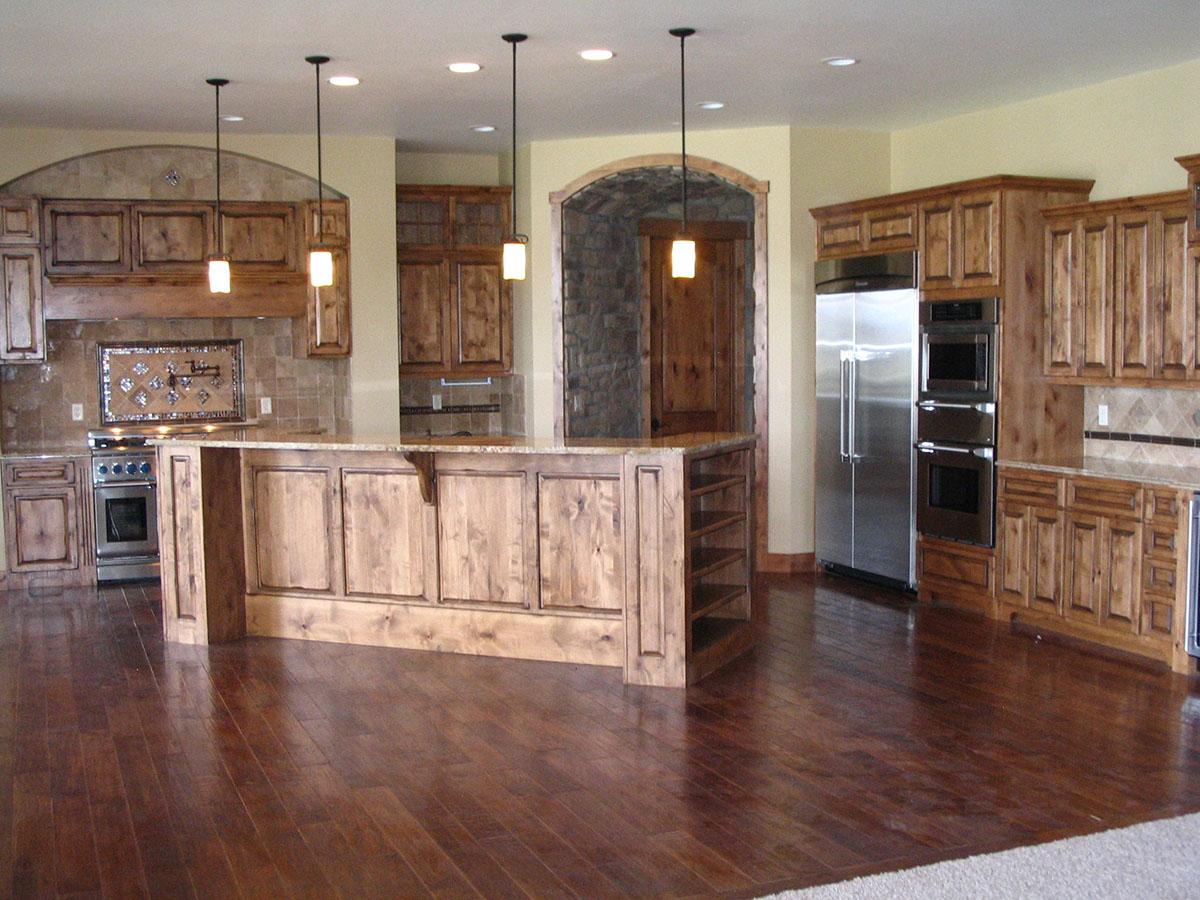 Kitchen with wood cabinetry, large island with granite countertop, stainless steel appliances, and stone archway.