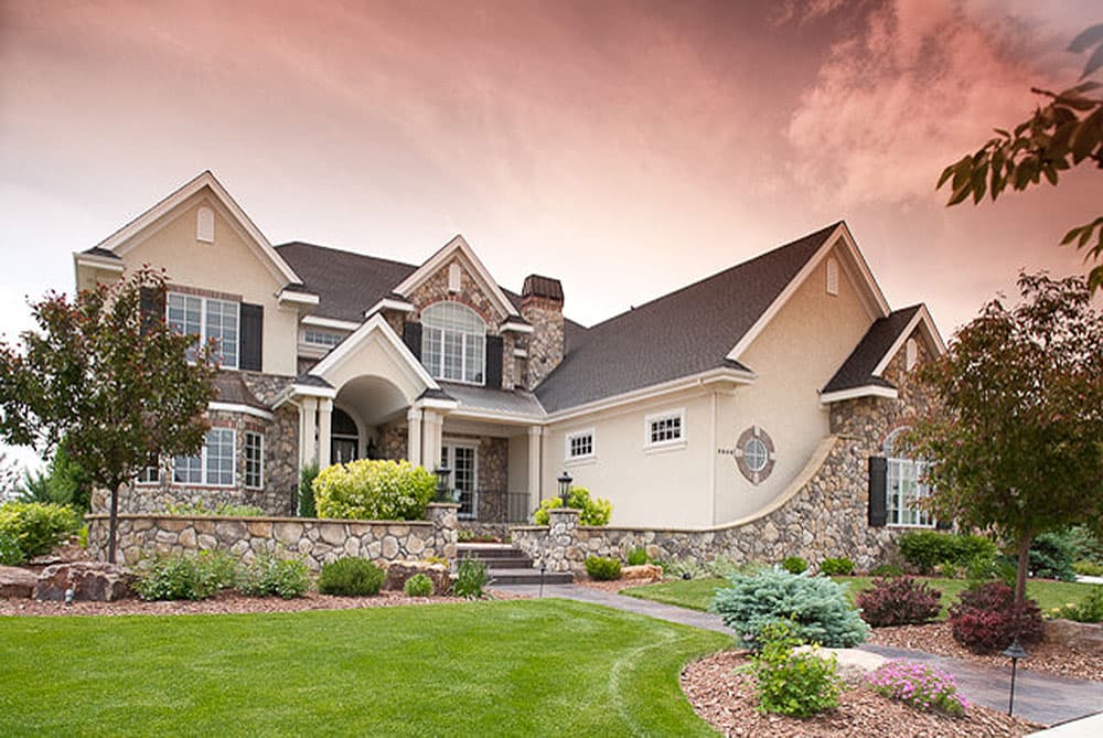 House plan exterior: Two-story home with stone accents, arched entry, multiple gables, and a rounded stone wall feature.