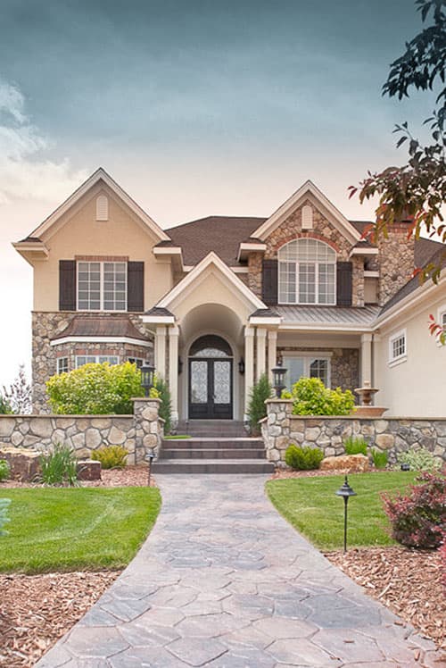 Two-story house plan exterior with arched entry, stone accents, multiple gables, and a winding stone walkway.