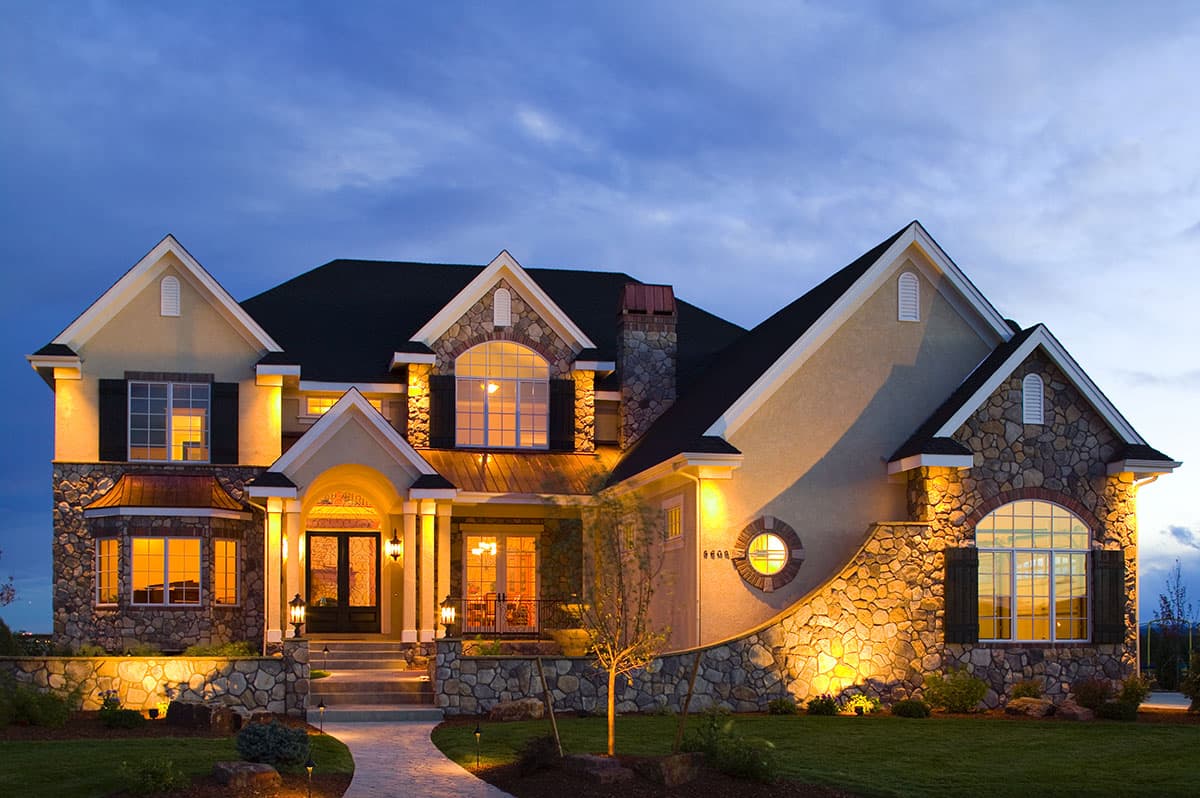 House plan exterior. Two-story home with stone accents, arched windows, and multiple gables. Features a covered entry and detailed rooflines.