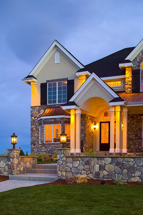 House plan exterior with stone facade, arched entryway with columns, gables, and multi-pane windows.