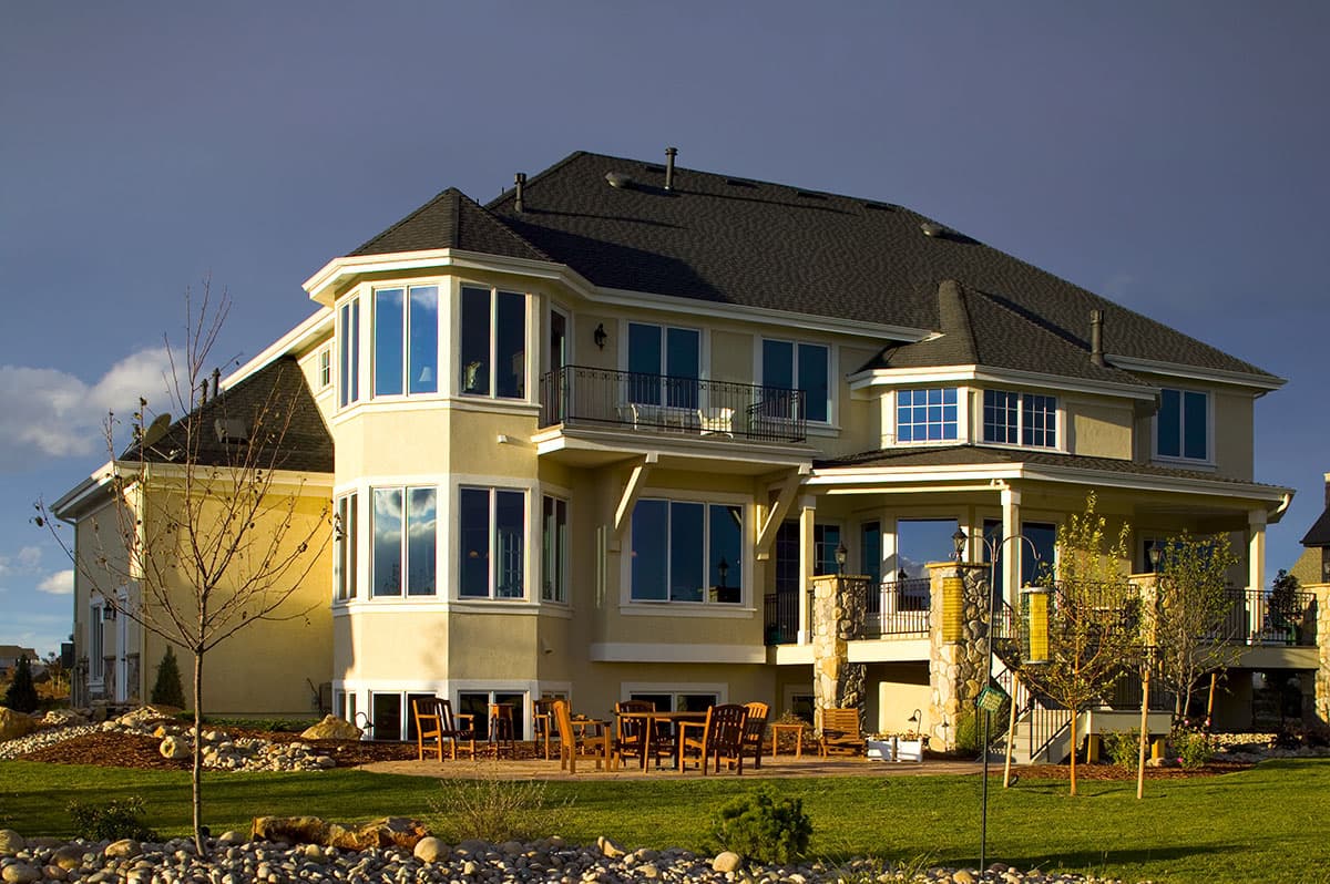 House plan exterior of a two-story home with bay windows, a second-story balcony, and a covered lower porch with stone columns.