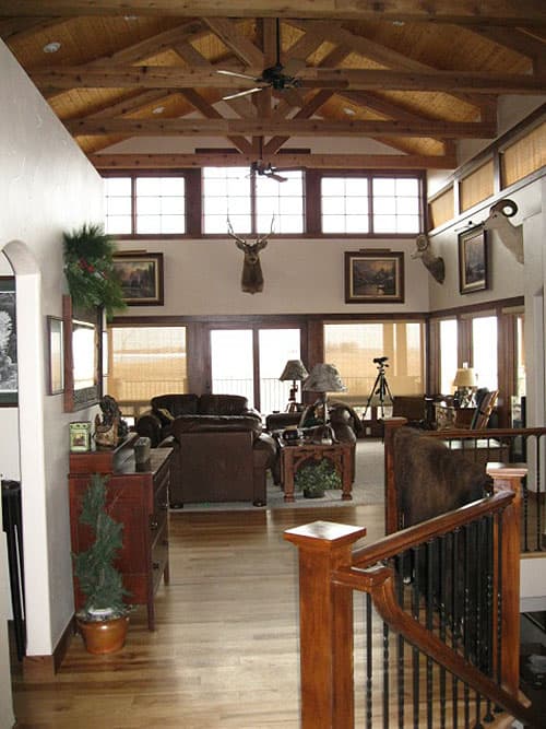 Great room with vaulted beamed ceiling, wood paneling, large windows, and a stone fireplace.