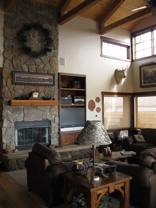 Great room with vaulted wood-beamed ceiling, stone fireplace, built-in entertainment center, and large windows.