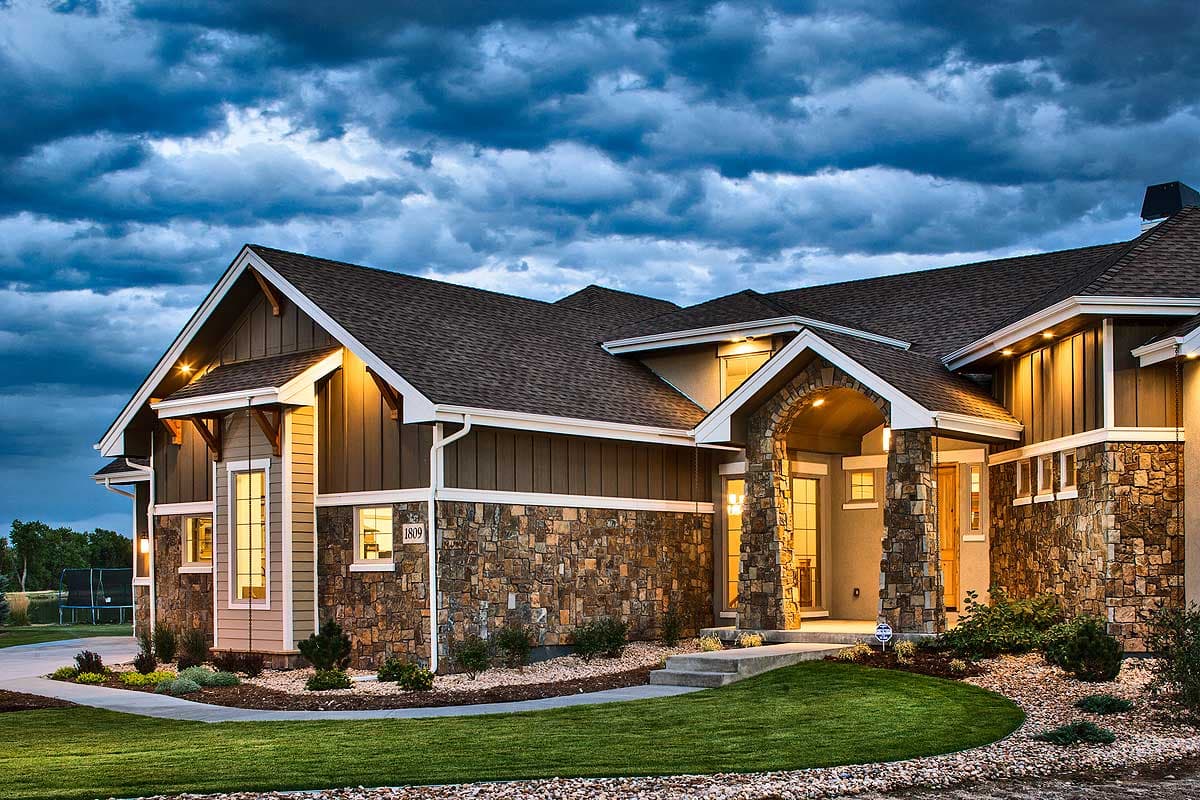 House plan exterior featuring stone and wood siding, multiple gables, and an arched stone entryway.