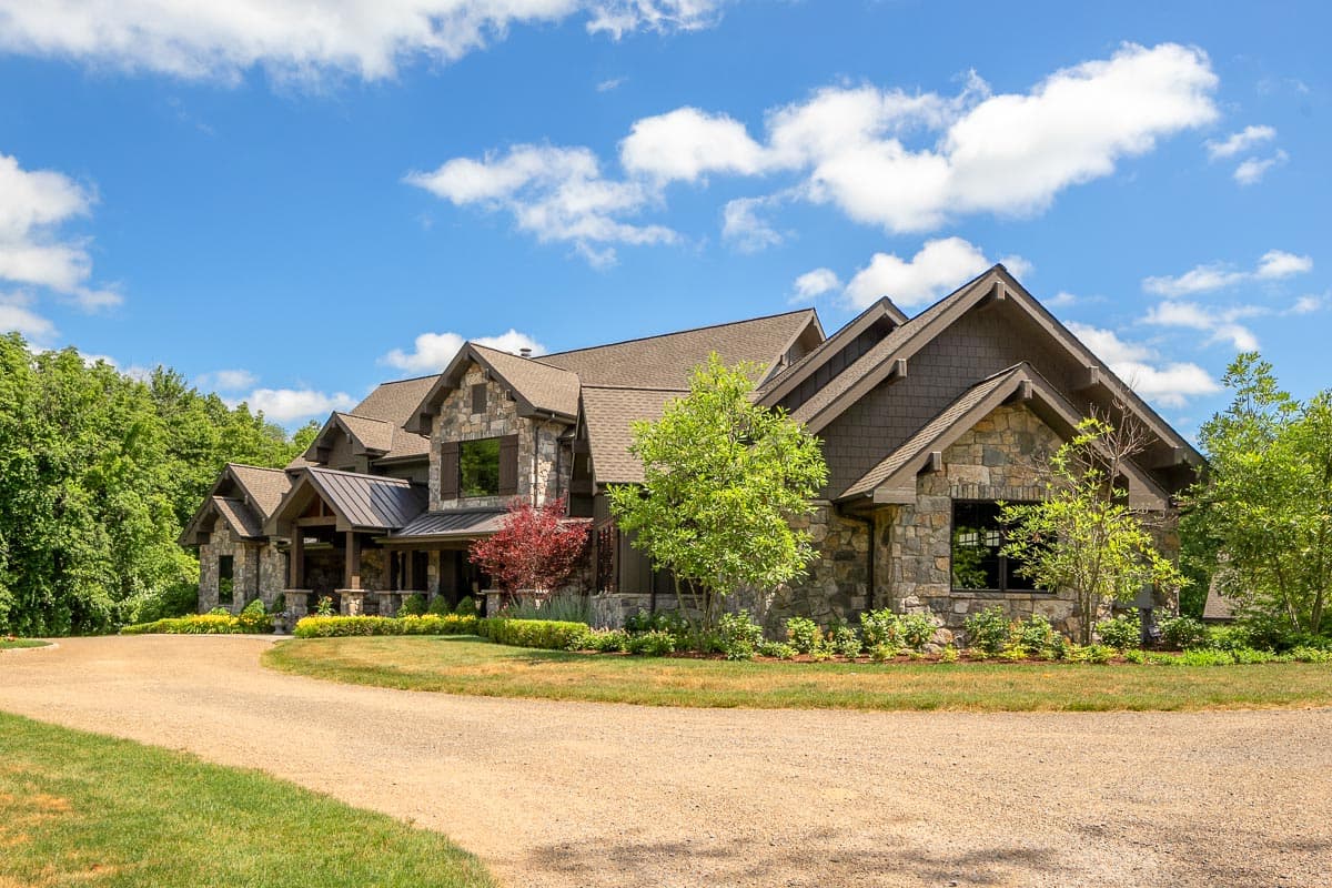 House plan exterior with stone facade, multiple gables, covered porch, and dark metal roof.
