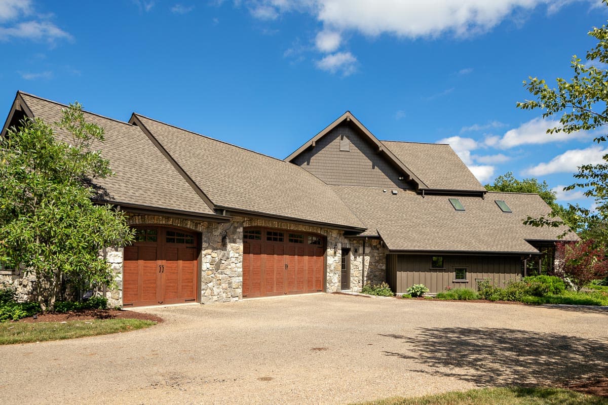 House plan exterior with stone facade, three wooden garage doors, and multiple gables under a shingled roof.