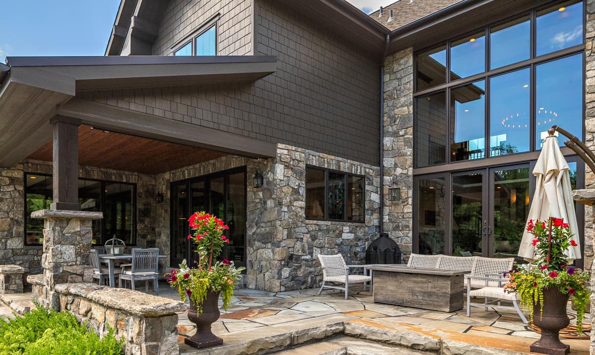 House plan exterior featuring stone and shingle siding, covered porch with wood ceiling, and large multi-pane windows.