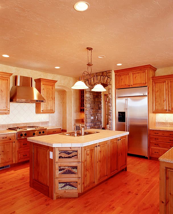 Kitchen with wood cabinets, large island with sink, stainless steel appliances, and stone archway.