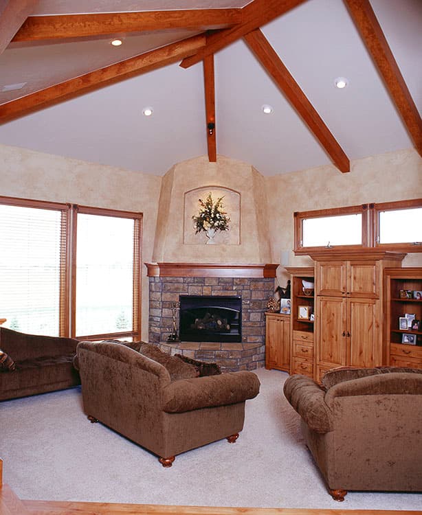 Living room with vaulted ceiling, exposed wood beams, stone fireplace, and large windows.