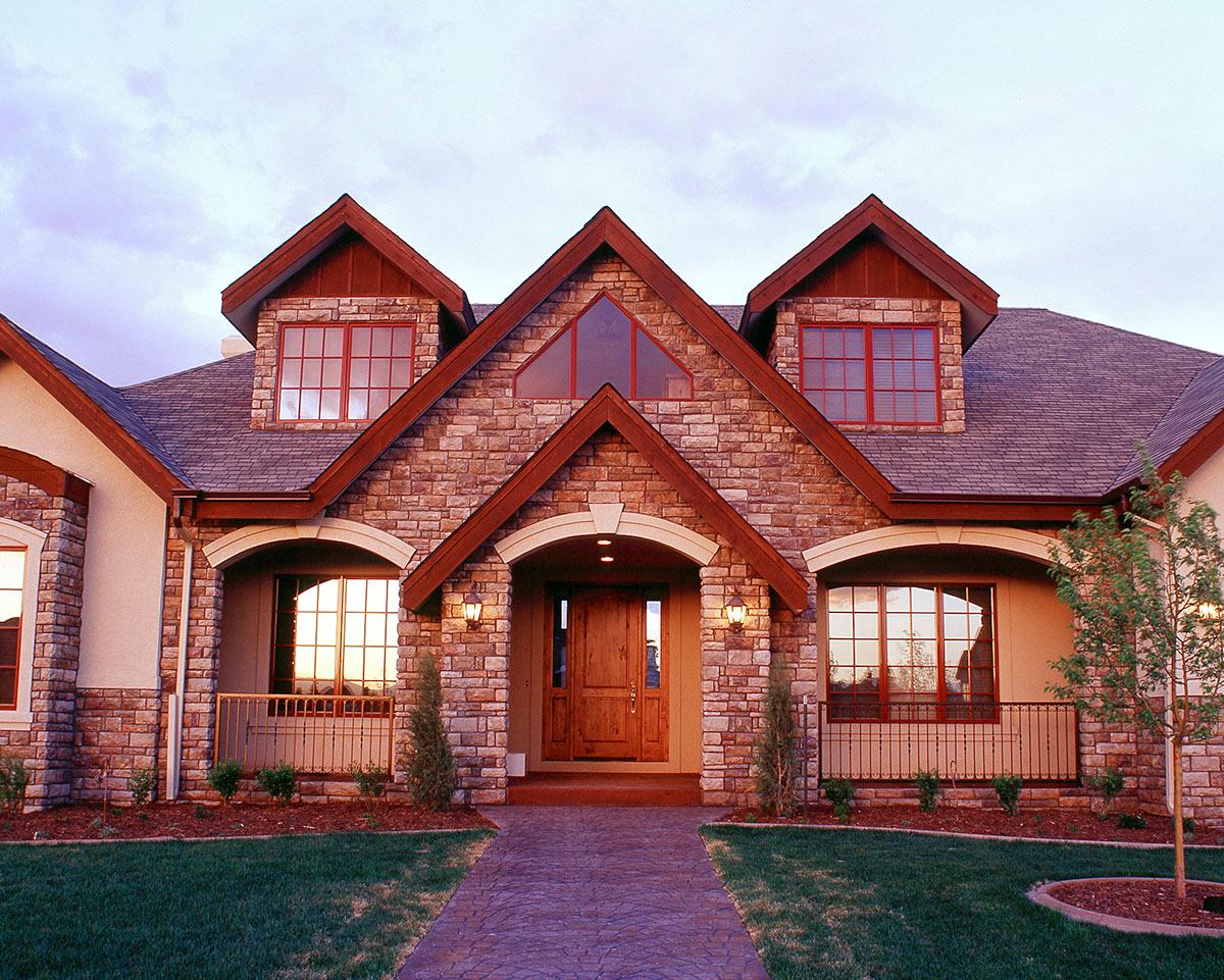 House plan exterior with stone facade, multiple gables, dormers, and arched entryway.
