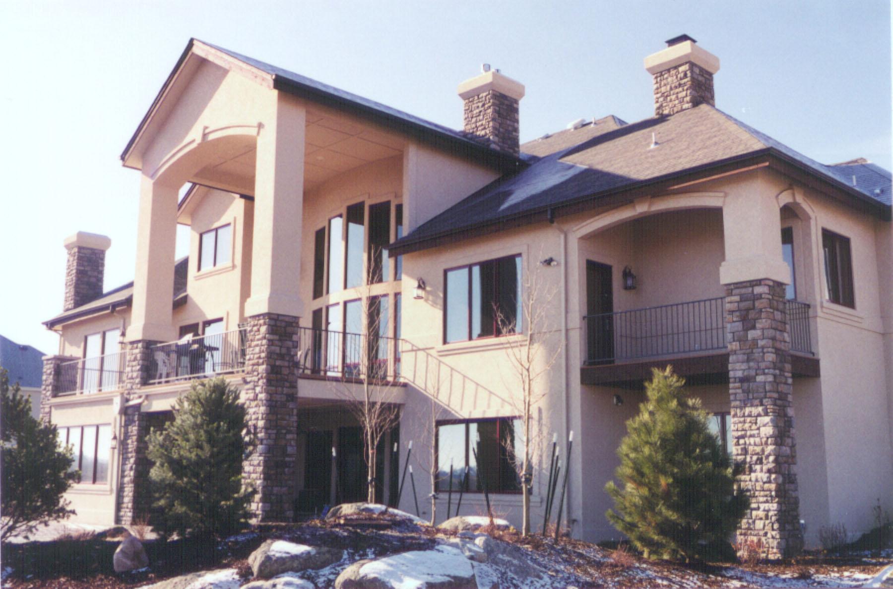 House plan exterior featuring multiple stories, arched balconies, stone-clad chimneys, and large windows.