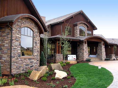House plan exterior with stone accents, wood siding, arched windows, gables, and covered entry.