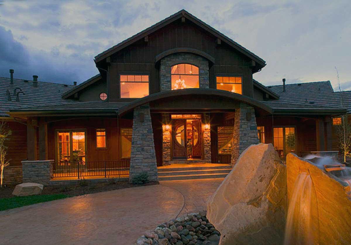 House plan exterior: Two-story home with arched entryway, stone pillars, covered porch, and multiple gables.