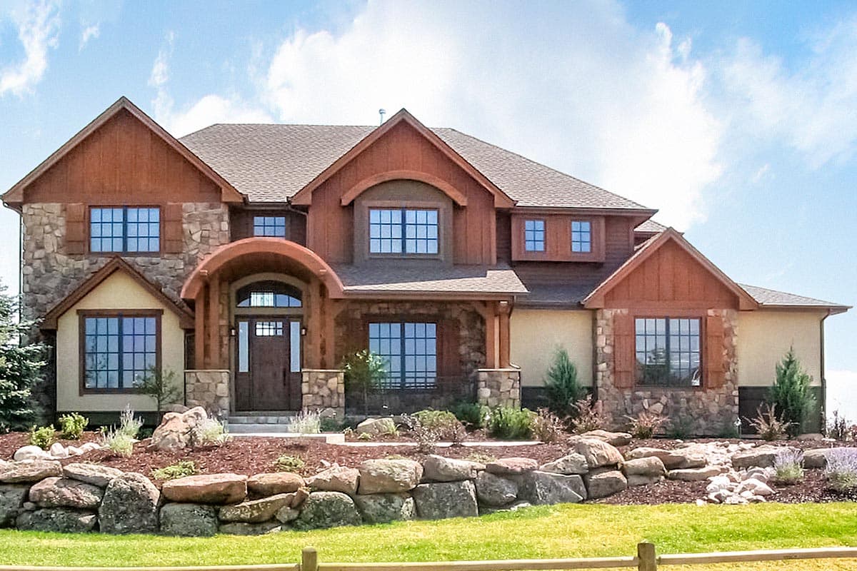House plan exterior with stone and wood siding, two stories, front entry arch, multiple gables, and a mix of window sizes and shapes.