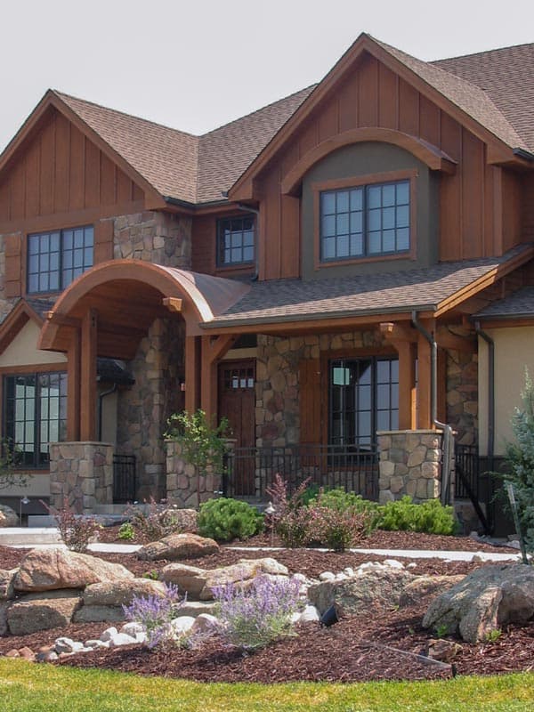 House plan exterior: Two-story home with stone and wood siding, gabled dormers, and covered entry with arched wood details.