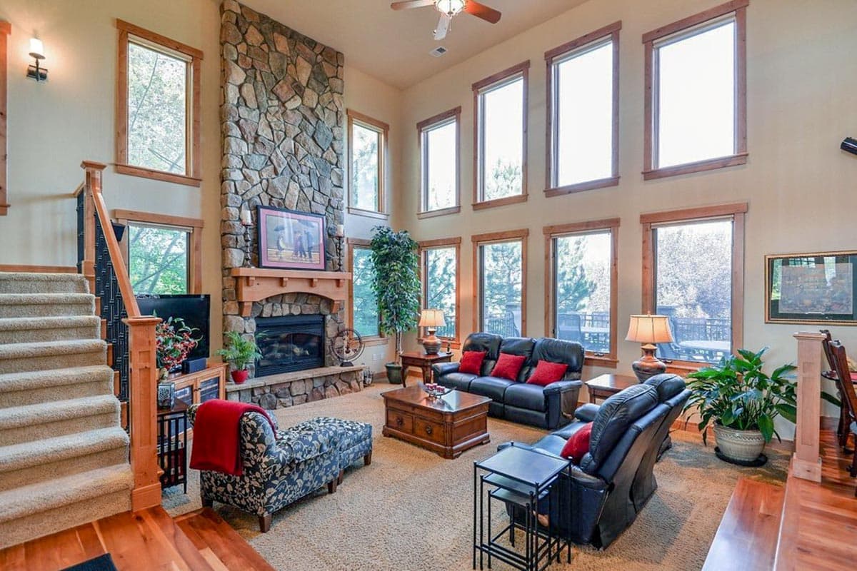 Living room with a floor-to-ceiling stone fireplace, two-story windows, and a carpeted staircase.