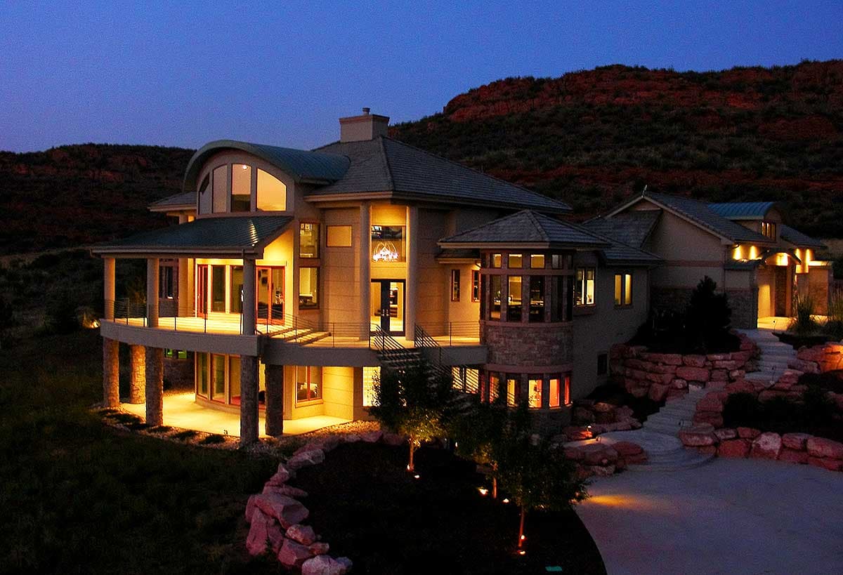 House plan exterior with a curved roofline, large windows, wrap-around porch, and stone accents.