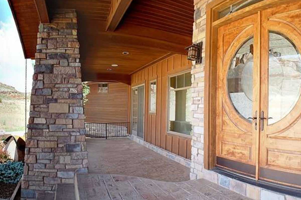 House plan exterior with stacked stone pillar, wood siding, and double wooden doors with circular glass. 
