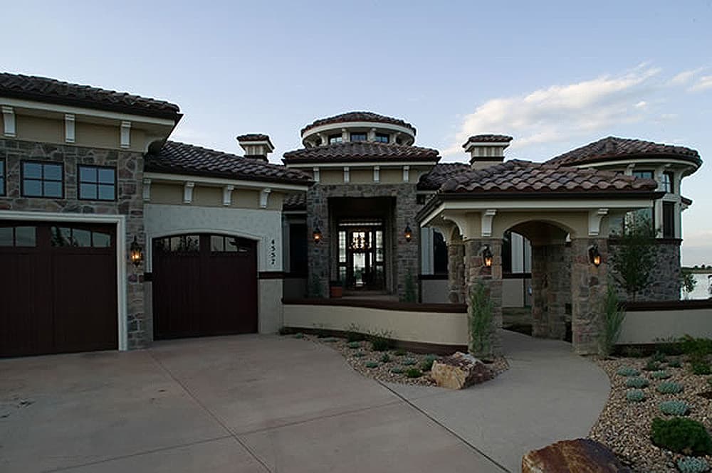 House plan exterior with Mediterranean style, three car garage, arched entryway with stone columns, and a central rotunda.