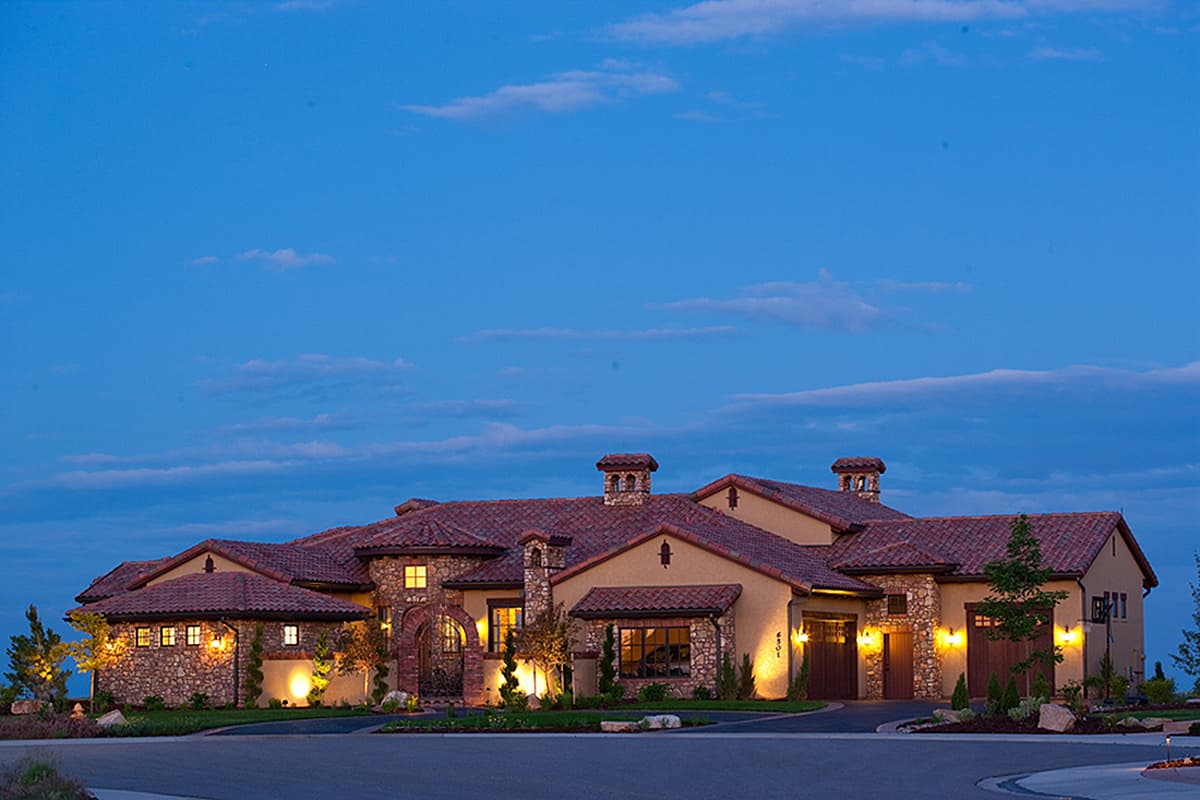 House plan exterior with stucco and stone facade, clay tile roof, arched entryway, and attached garage. Multiple chimneys are visible.