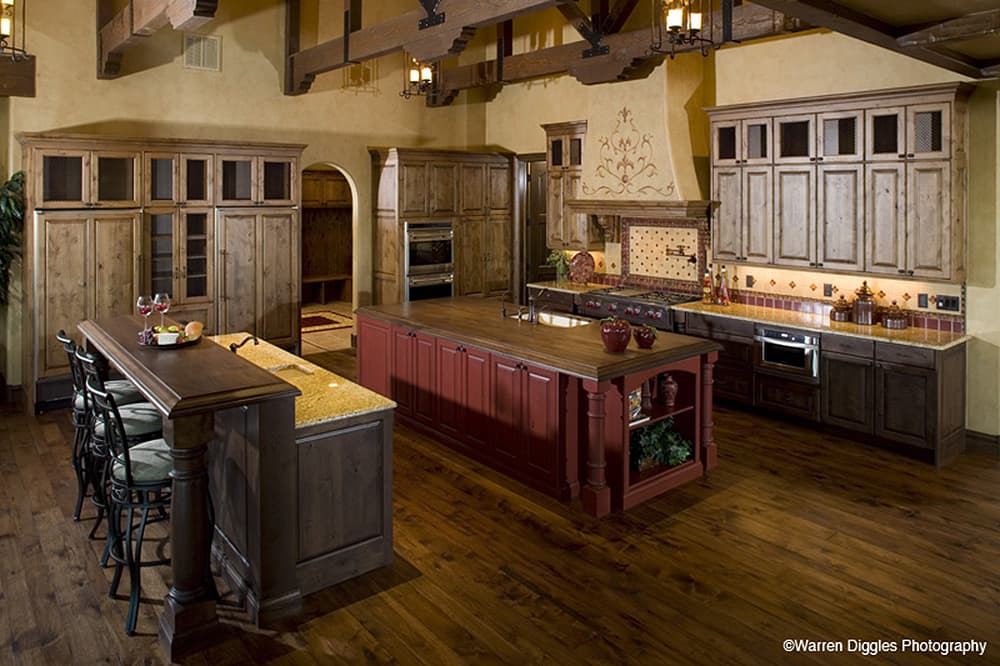 Kitchen with two islands, extensive wood cabinetry, exposed beams, and a range with decorative hood.