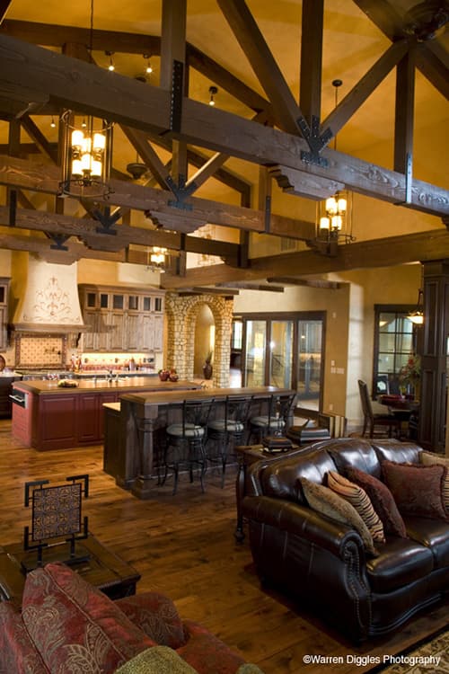 Interior view of a great room with vaulted wood-beamed ceiling, stone archway, kitchen island, and seating area.