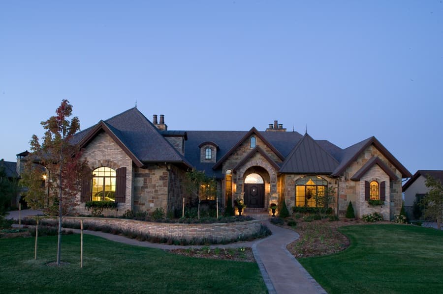 House plan exterior: Stone and brick single-story home with arched entry, multiple gables, and prominent chimneys.