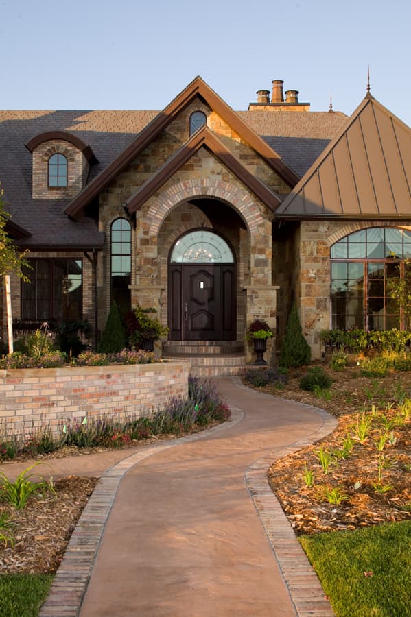 House plan exterior with arched stone entryway, brick accents, dormer window, and metal roof.