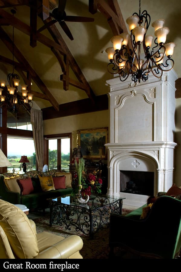 Great Room with ornate stone fireplace, wood ceiling beams, chandeliers, and large windows with scenic view.