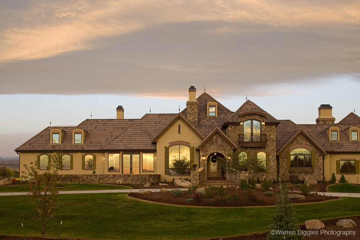 House plan exterior featuring a multi-story French Country style with stone accents, prominent gables, dormers, and arched windows.