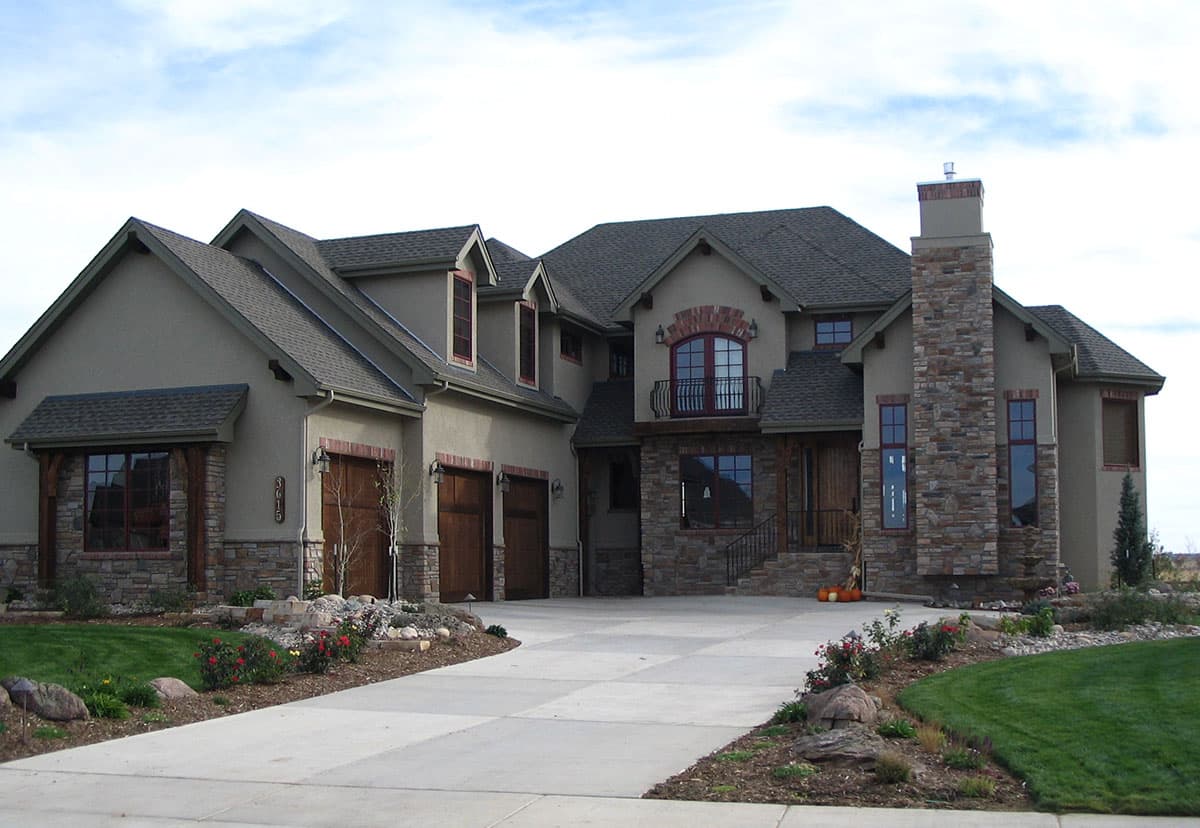 House plan exterior with stone accents, multiple gables, and a brick chimney. Two-story, with a three-car garage and dormers.