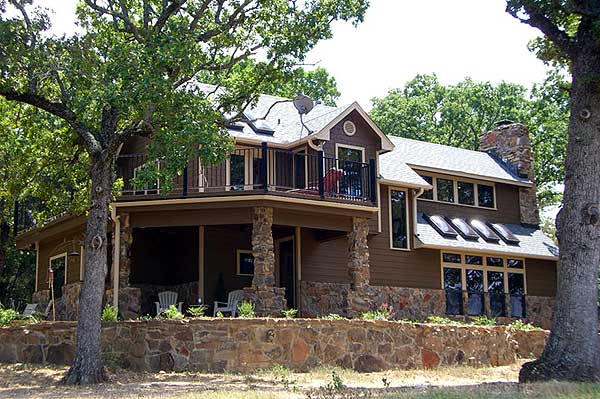 House plan exterior: Two-story home with covered porch, stone pillars, balcony, dormers, and stone foundation.