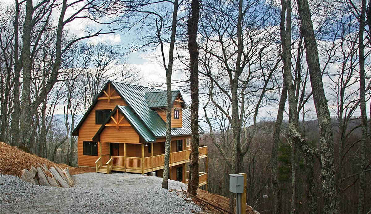 Two-story wooden house plan with a green metal roof, prominent gables, and a wraparound porch.