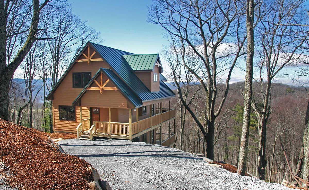 House plan exterior: Two-story rustic cabin with exposed rafter tails, covered porch, and metal roof.