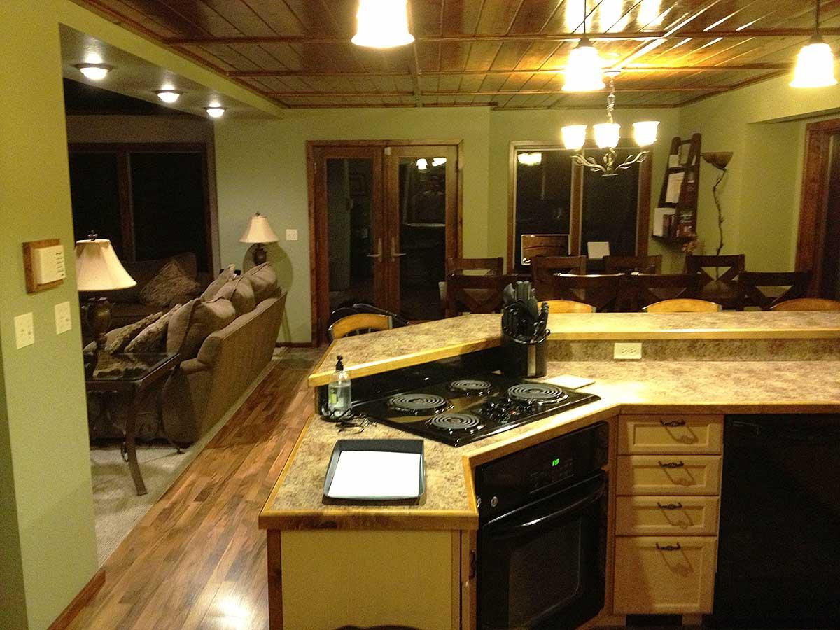 Kitchen area with island, stove, and cabinetry, opening to dining and living areas with wood ceilings.